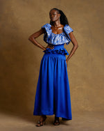 Load image into Gallery viewer, Woman wearing a blue outfit with ruffled top and wide-leg pants against a brown background