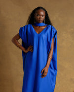 Load image into Gallery viewer, Woman wearing a blue dress against a brown background