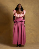 Load image into Gallery viewer, Woman wearing a pink dress with ruffled top and skirt against a gold background

