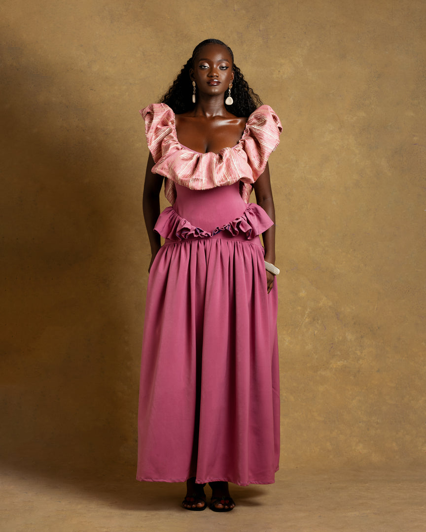 Woman wearing a pink dress with ruffled top and skirt against a gold background